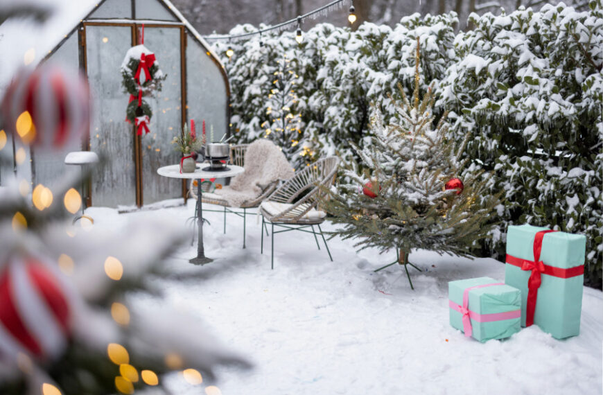 Ein weihnachtlich geschmückter, verschneidter Garten mit Gewächshaus.