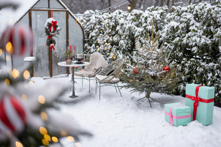 Ein weihnachtlich geschmückter, verschneidter Garten mit Gewächshaus.